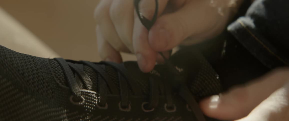 A person quickly ties the laces on the black sneaker