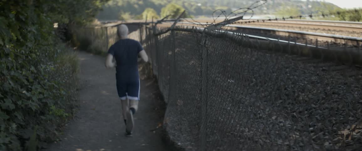Man jogs down a path near a chain link fence