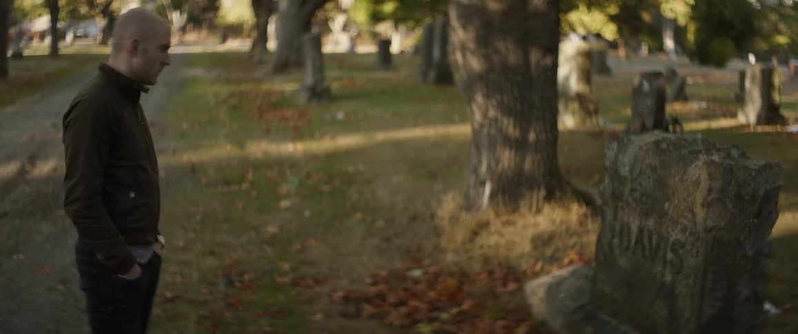 A man stands in a cemetery looking at an old tombstone