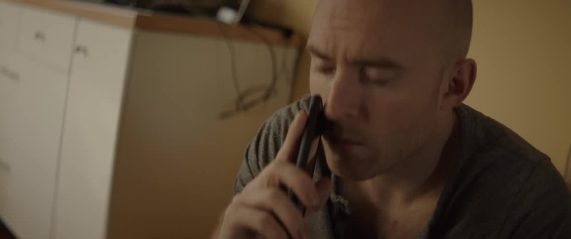 A man is rubbing his face as he finishes a phone call while sitting indoors in daylight