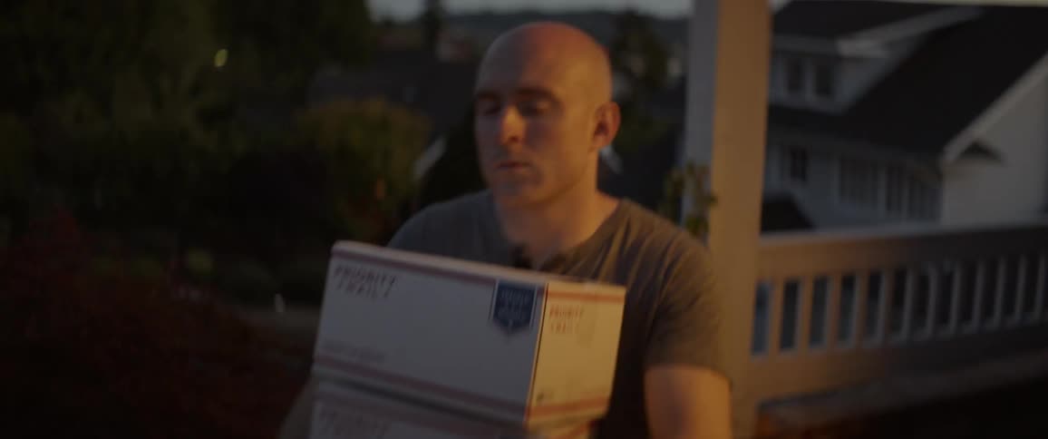 A man walks on a porch carrying three boxes
