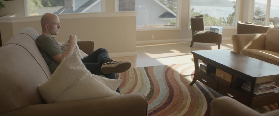 The man is sitting on the couch holding his pillow