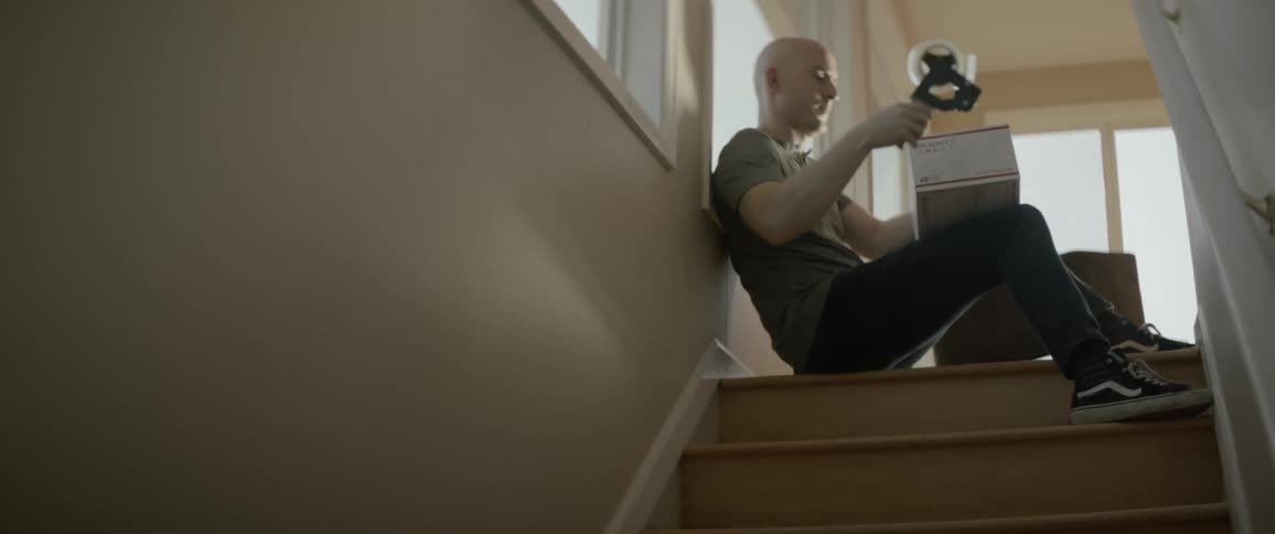 The man sits at the top of the stairs taping a box shut