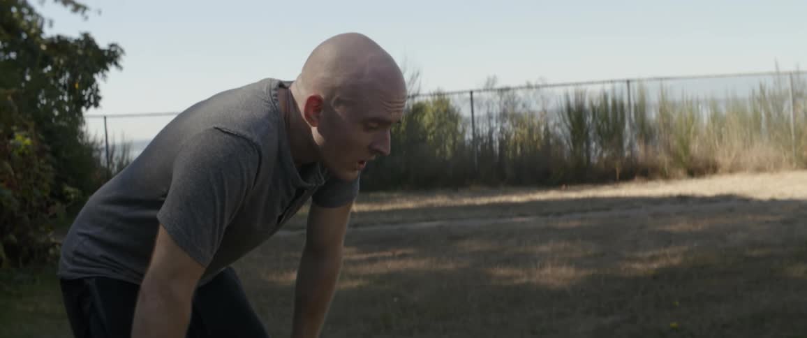 Bald man bends over with his hands on his knees as he stands outdoors