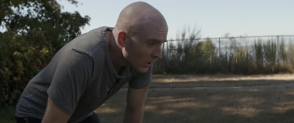 A man is bent over breathing heavily outside on a sunny day