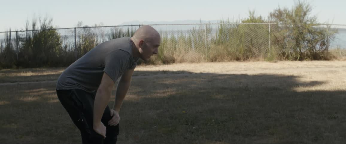 Man leans over with his hands on his knees breathing heavily in a field