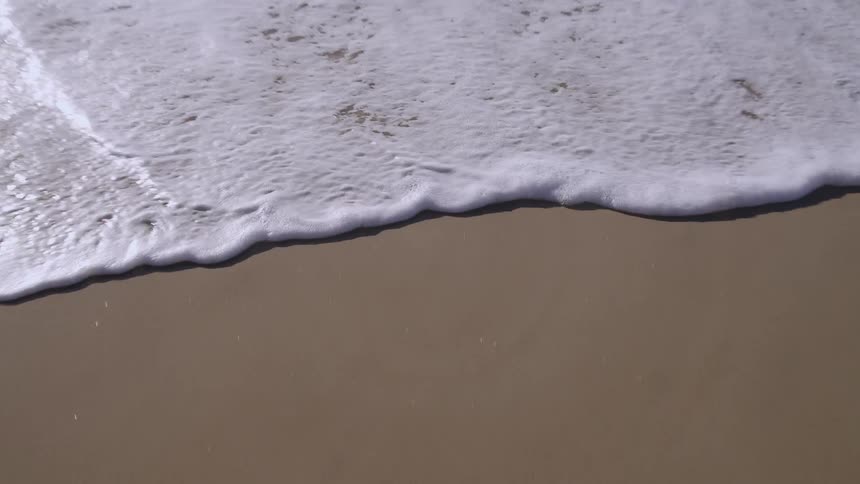Foamy ocean wave breaks against the sand on the beach