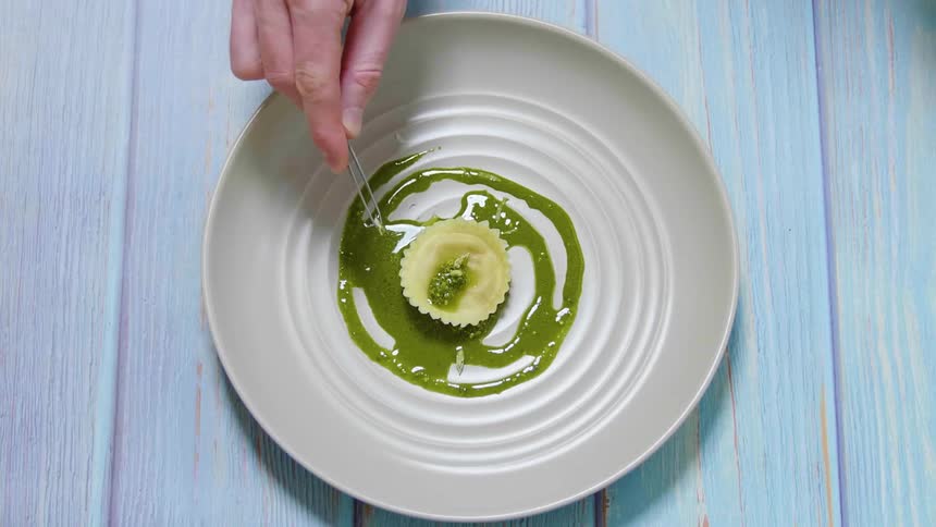 Close up of a chef garnishing a dish using small stainless steel pincers