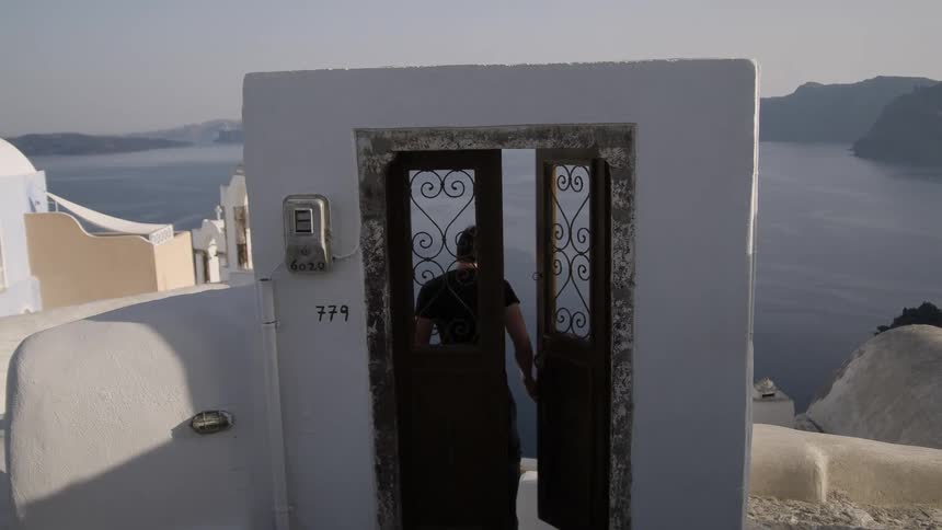 A man with a carrier bag walks through a door on a rooftop overlooking the sea