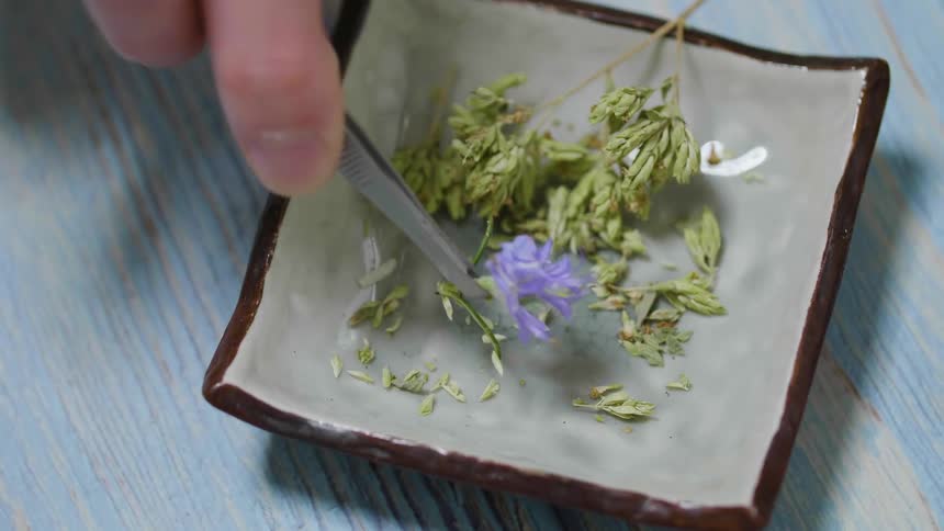 A close up of a person using tweezers to pick upa flower from a plate