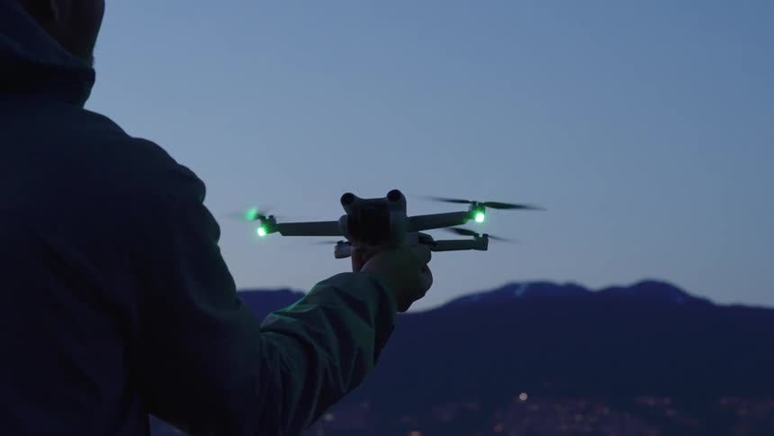 A flying drone lands in the outstretched hand of a man standing outdoors in the evening