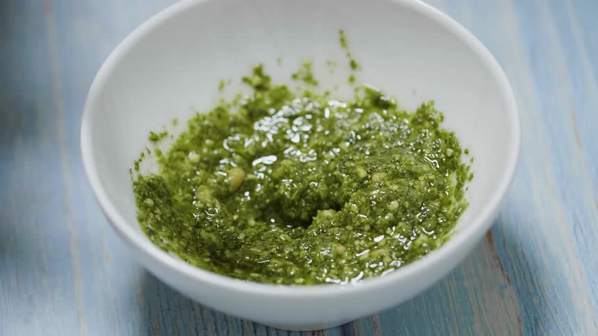 An adult is spooning some pesto sauce out of a white bowl