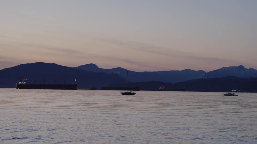 A couple small boats and a tanker ship are anchored with mountains in the background