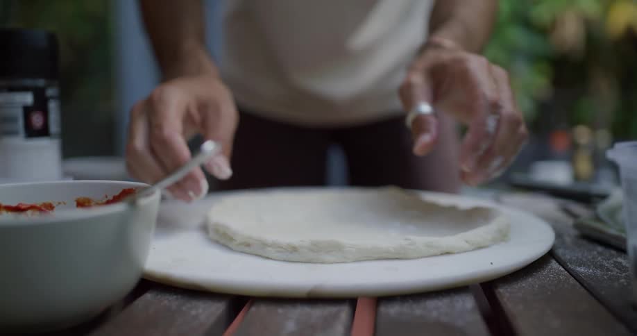 A person sprinkles seasoning on dough before lifting the dough from the cutting board