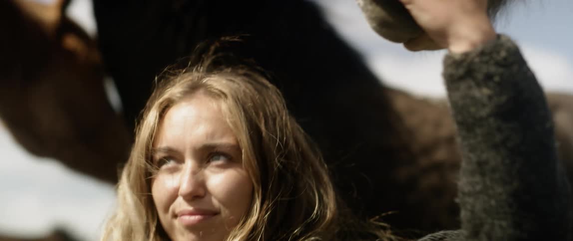 A woman is stroking a horse's muzzle outside on a windy day