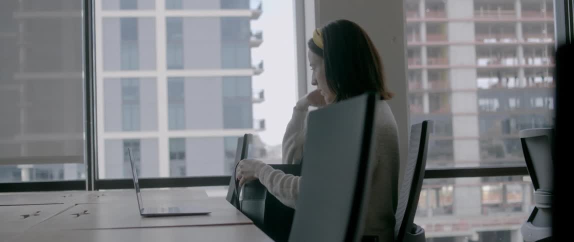 Woman who sits at the table opens laptop in the office building during daylight