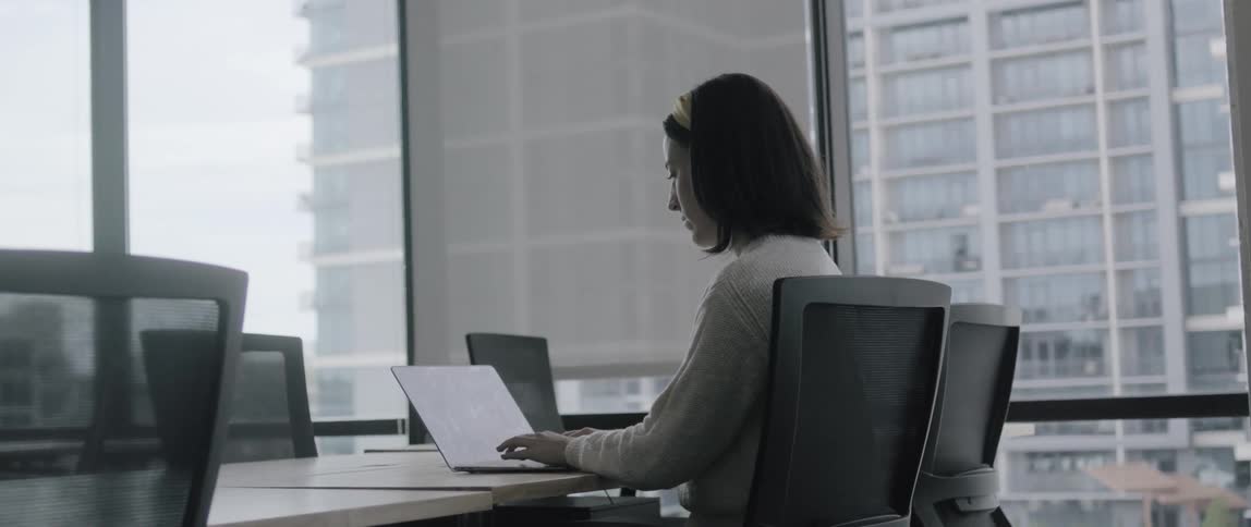 A white woman sits at a desk in an office and types on a laptop