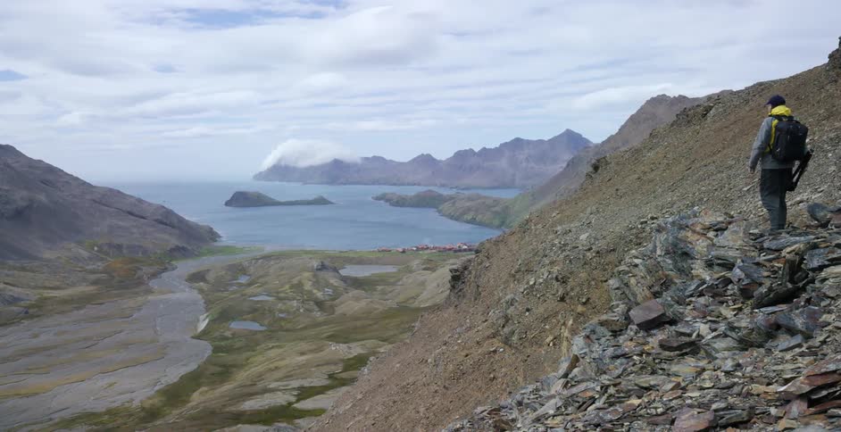 A hiker stopping at the edge of a rocky cliff to look out over a body of water below