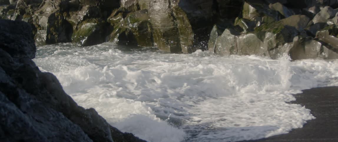 Ocean waves break and splash against the rocks on a sunny day