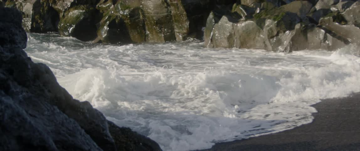 The large waves crash against the circle of rocks