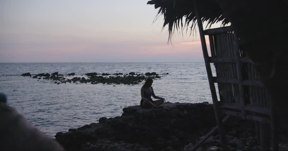 A person sitting cross legged and meditating on a beach at sunrise