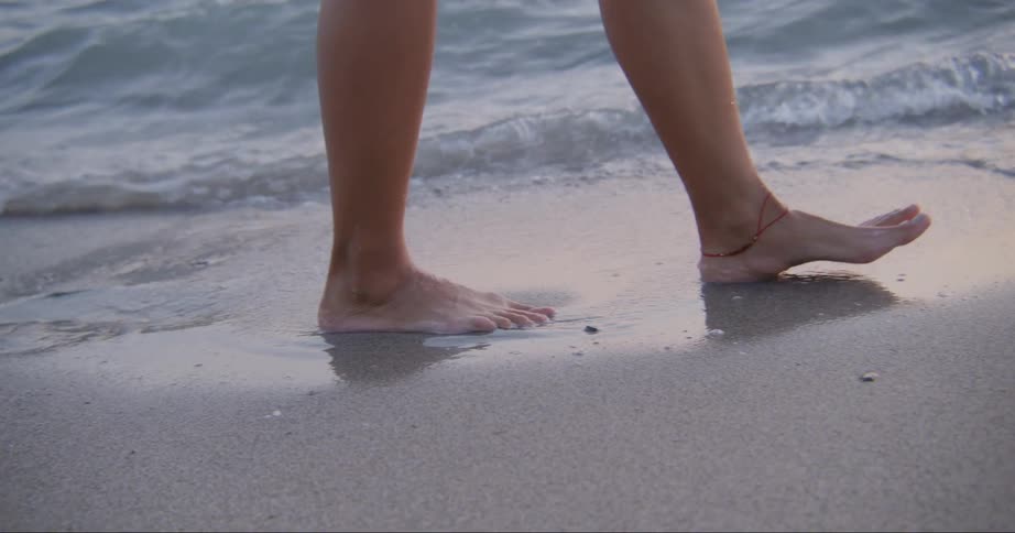A woman walks barefoot along the beach