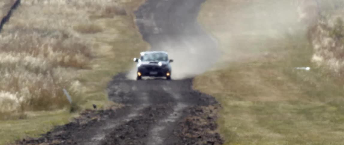 A car kicking up dust while driving on a rural dirt road in the daytime