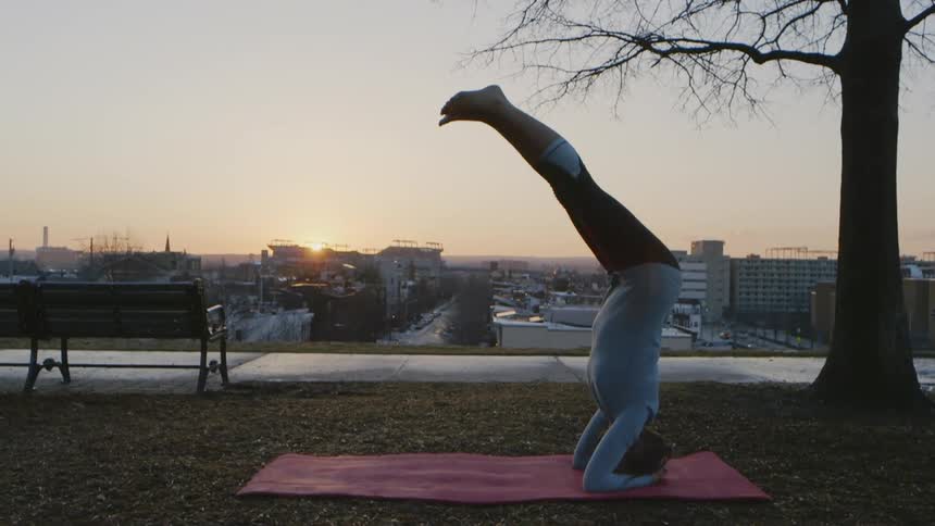 The woman is doing yoga on a hill above the city