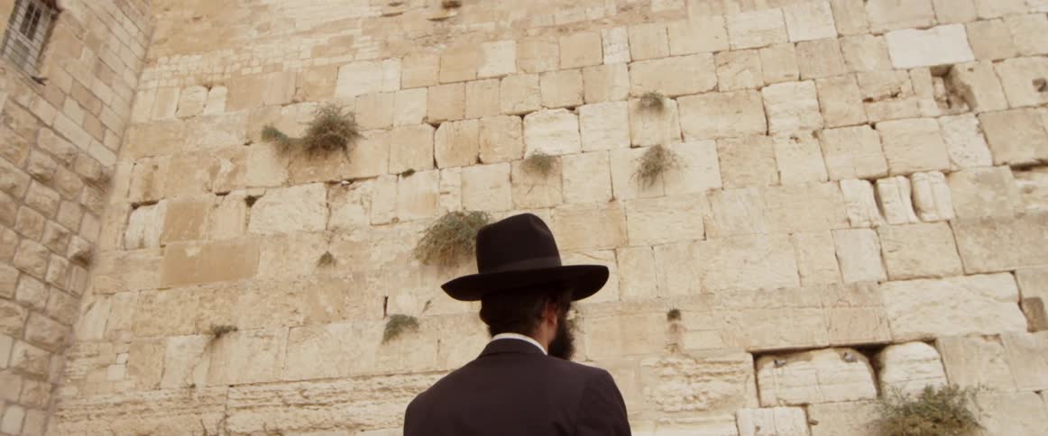 A jewish man is standing in front of the wailing wall
