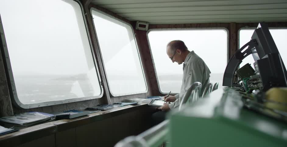 Man writing into his notebook in a ship's control cabin