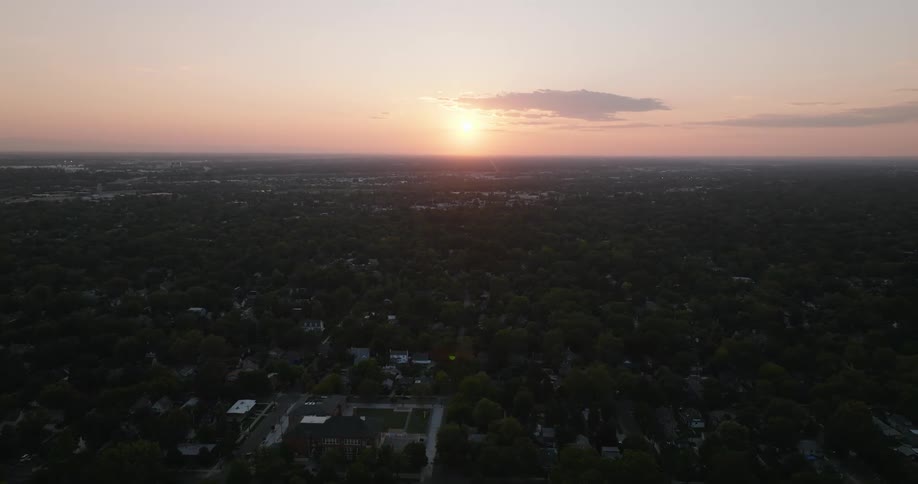 Moving over a neighborhood with houses and trees along the streets as the sun shines brightly on the horizon