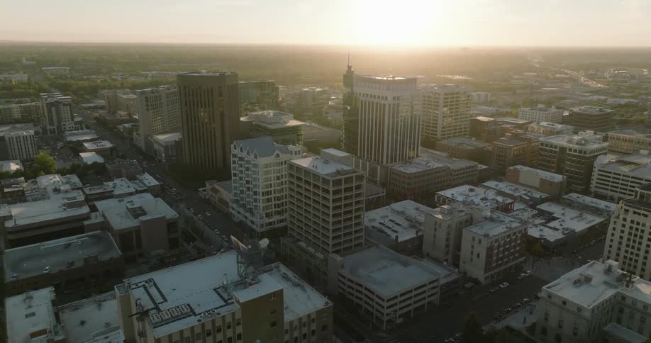 Towers and buildings stand tall in a metropolitan city as traffic moves on the streets and the sun shines brightly on the horizon