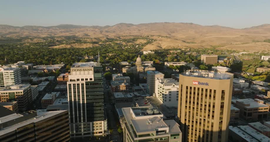 The sun shines on city buildings and towers with mountains in the distance and a domed building on the edge of town