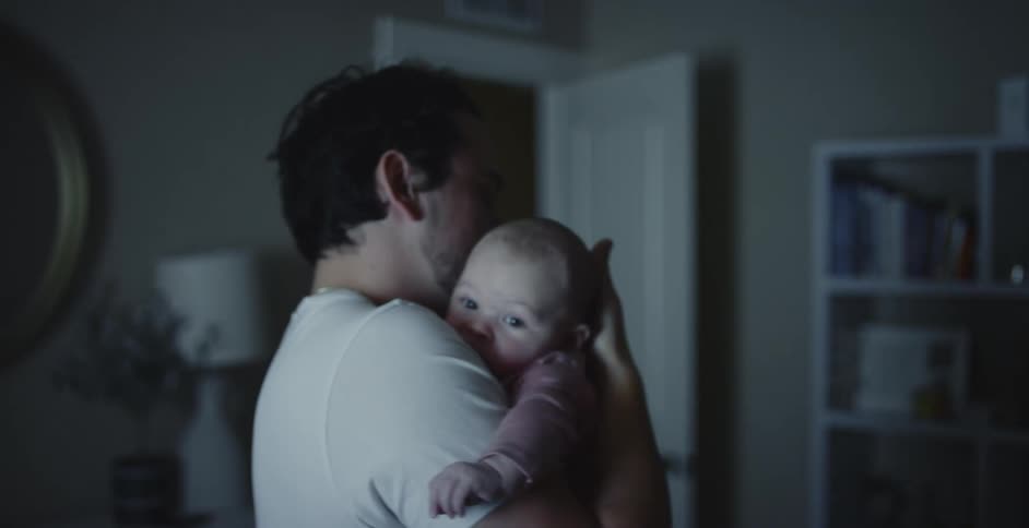 Father with white shirt rocks newborn baby in his arms in room