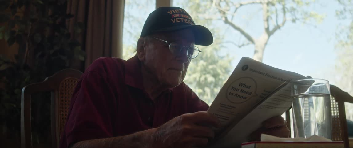 Man sitting at dining table reads from a booklet near a large window