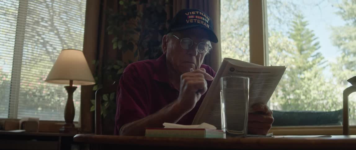 A man reads a magazine while sitting down with a glass of water