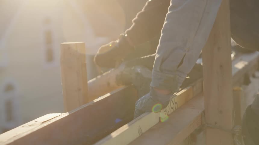 A construction worker moves a pipe onto slabs of wood on a rooftop