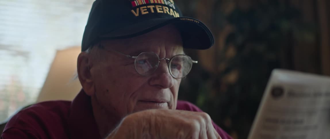 An elderly man sits at home and reads a newspaper