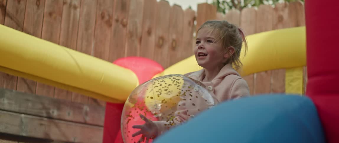 Sister holds clear ball as she and brother play in bounce house in backyard