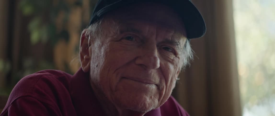A man smiles while sitting next to a window