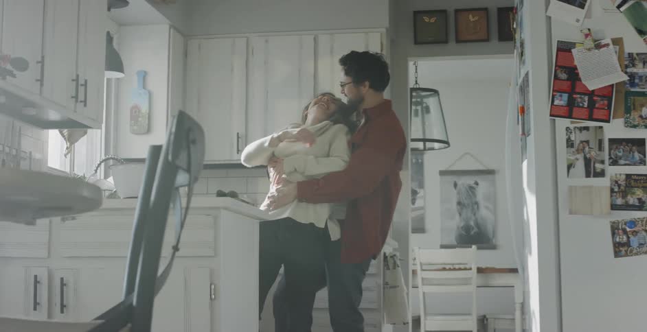Man catches running woman in kitchen and hugs her with a smile