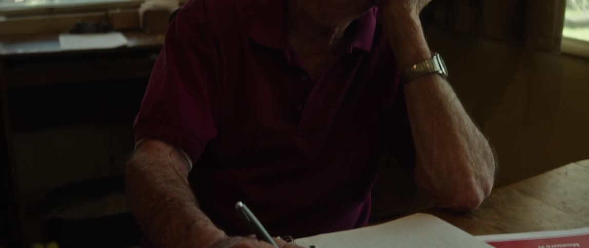 A man is sitting indoors and writing on paper