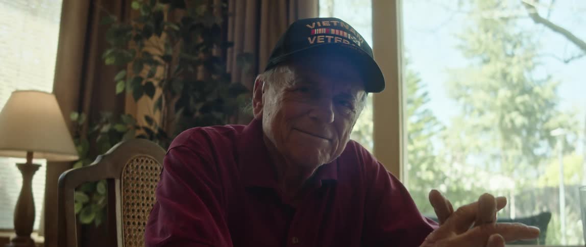 An older man sitting at his dining room table smiling and posing