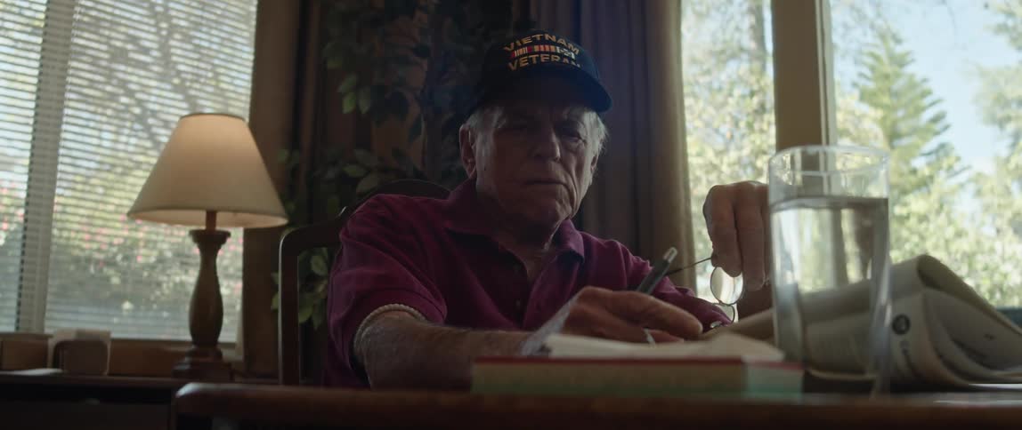An elderly man at home reads a paper and then takes his glasses off as he thinks