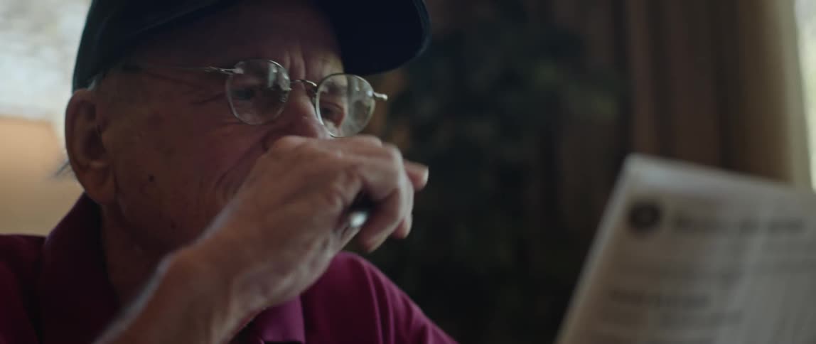 An elderly man sits at home and reads a newspaper