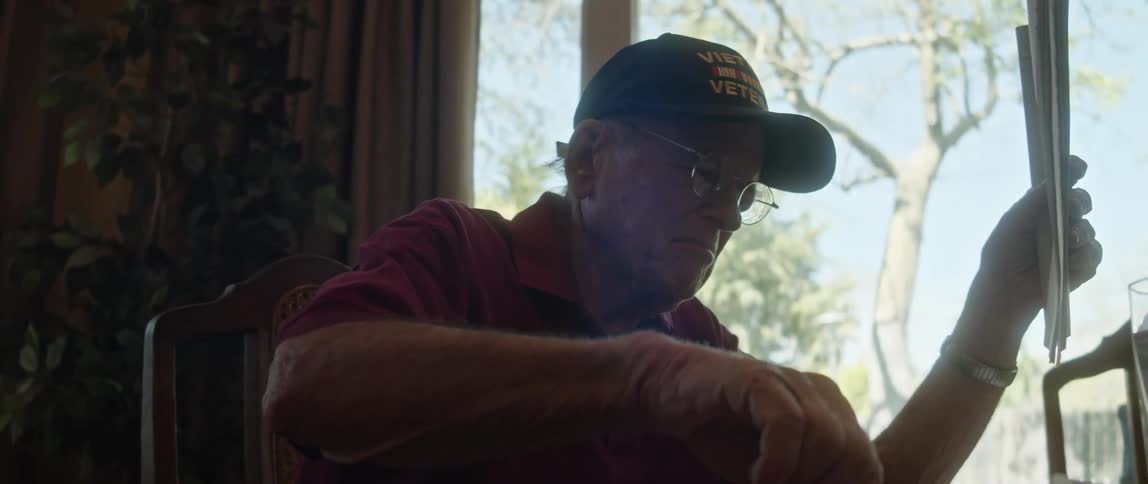 An elderly man at home flips through some papers and then picks up a pen