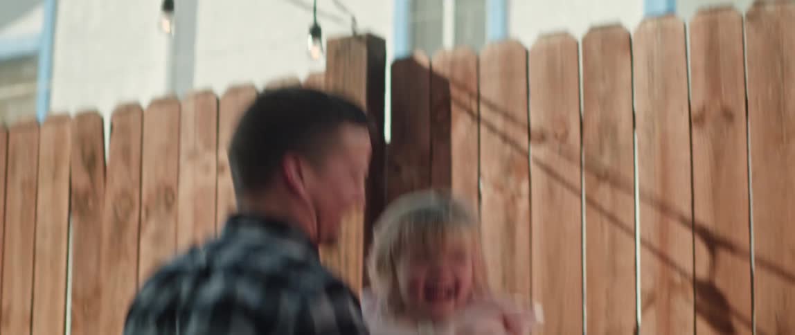 Father throws and catches his young daughter in house yard near fence