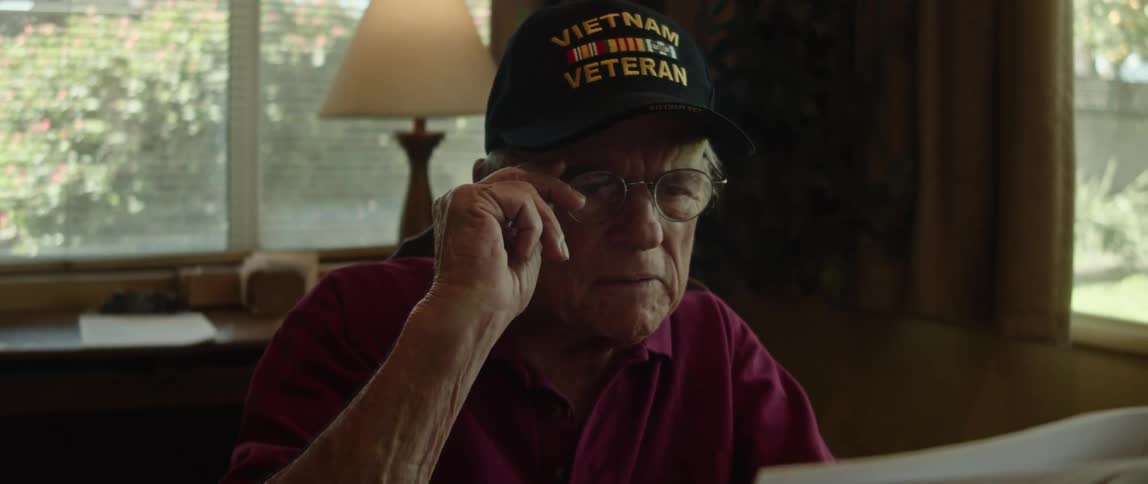 An elderly man at home reads the newspaper and then takes his glasses off as he thinks