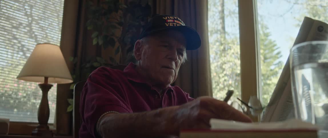 An older man is sitting at a desk while reading a magazine and writing