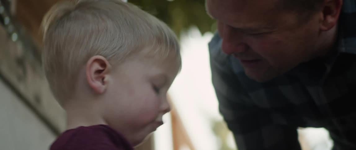 A man stands outside a house and talks with his young son